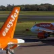 Close-up view of an orange EasyJet tail aircraft on the tarmac with another jet in the background at the gate/stand area of an airport runway.