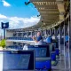 Man swinging a golf club in a Topgolf driving range bay under a bright blue sky, with several bays and screens nearby
