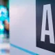 Sign reading 'AI' on a wall at a tech event with blurred blue-lit attendees in the background