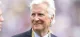 Smiling older man in a dark suit and blue tie, wearing a FIFA World Cup 2025 lanyard.