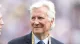 Smiling older man in a dark suit and blue tie, wearing a FIFA World Cup 2025 lanyard.