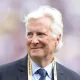 Smiling older man in a dark suit and blue tie, wearing a FIFA World Cup 2025 lanyard.