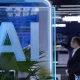 Glass panel with large blue 'AI' lettering in a tech expo or office setting, man in suit blurred in background